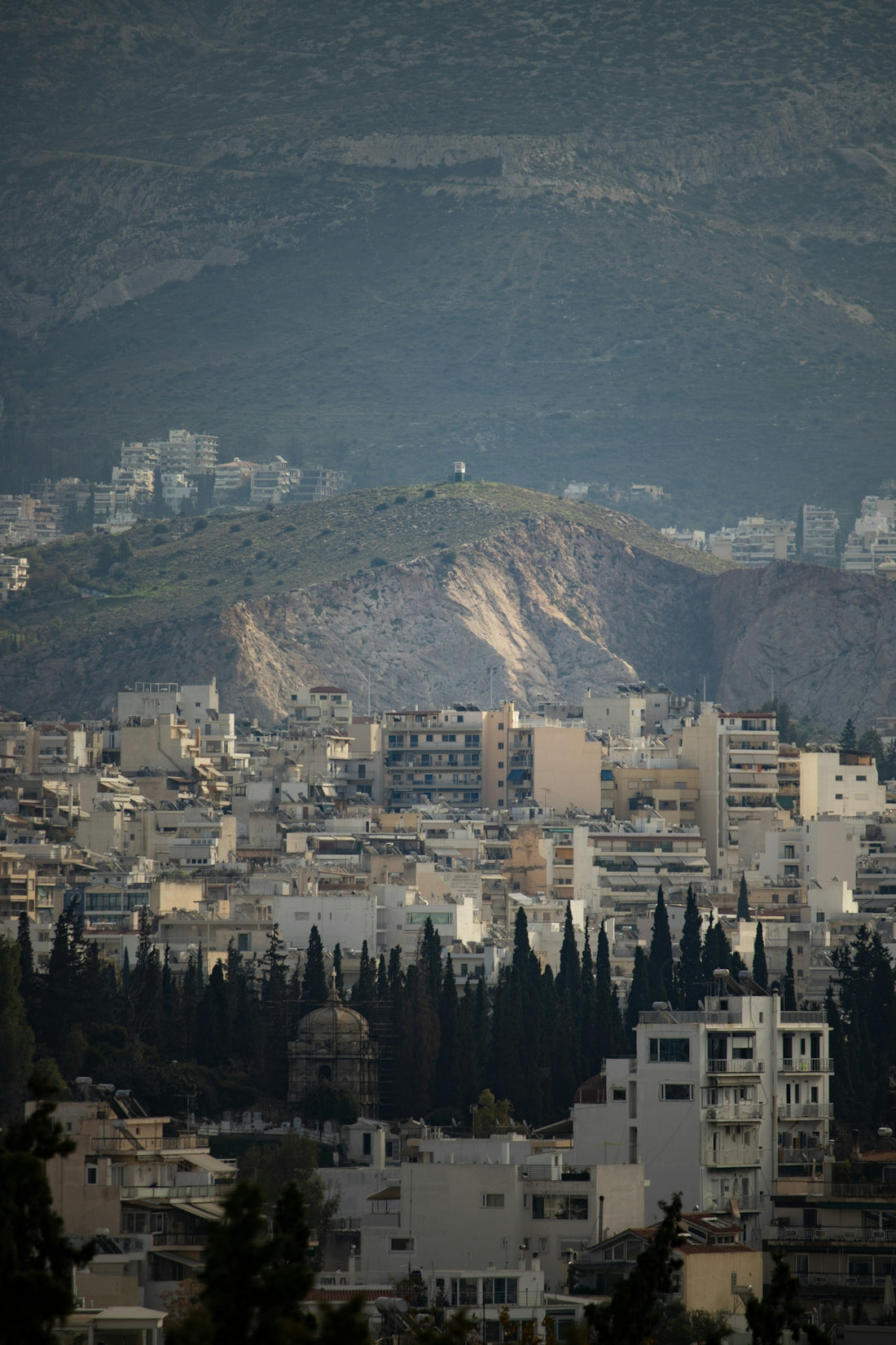 Cityscape with buildings and distant mountains under hazy sky.
