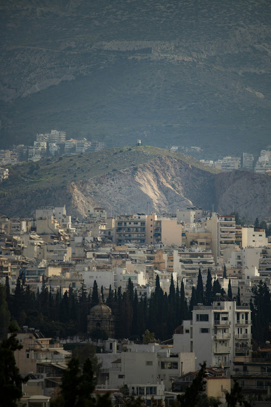 Cityscape with buildings and distant mountains under hazy sky.