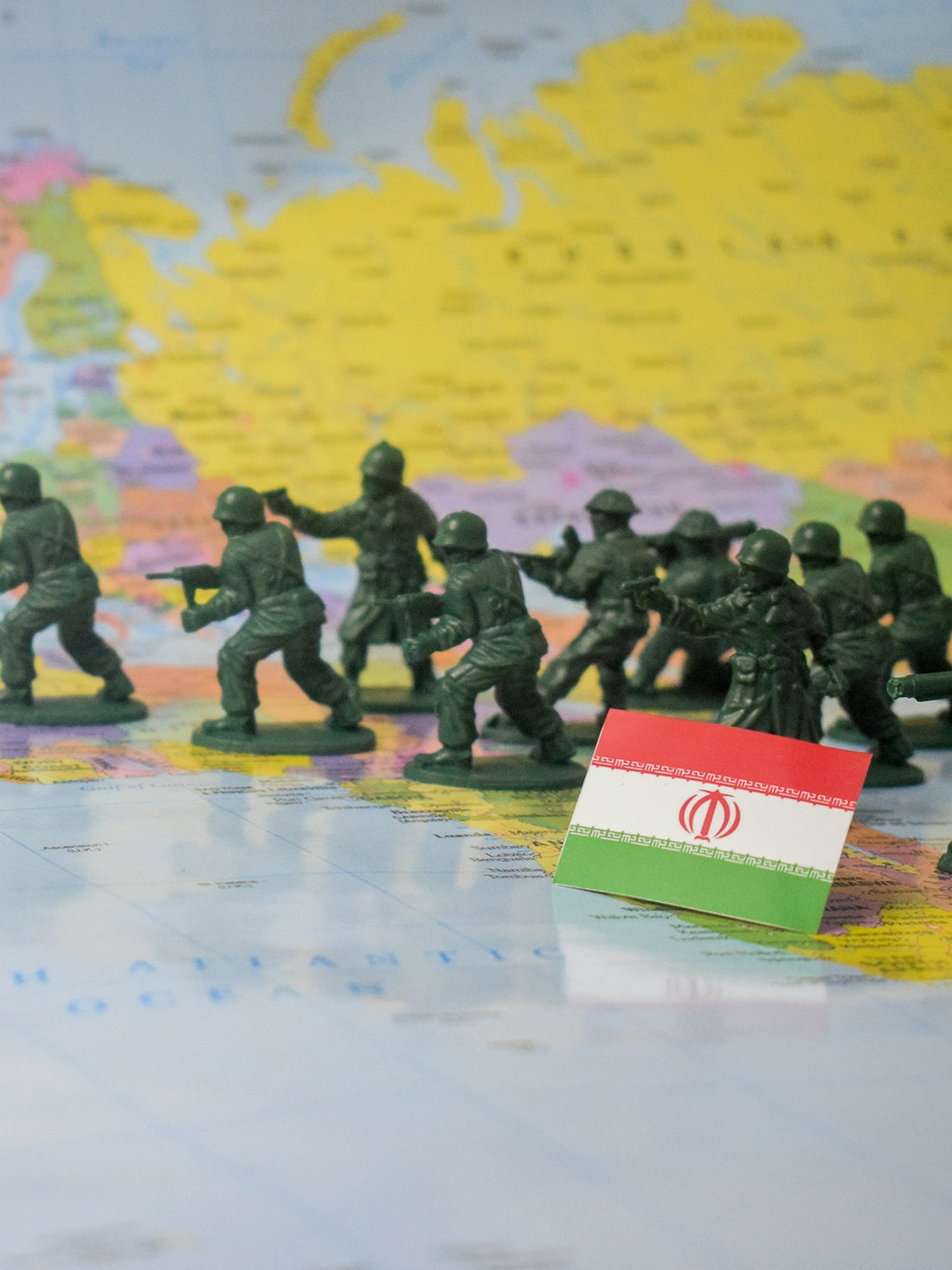 Toy soldiers advance across a world map near iran's flag